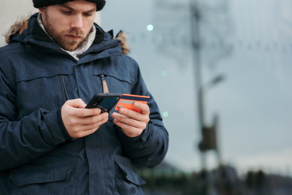 Free Crop concentrated man in warm clothes entering credentials of credit card on mobile phone while standing in street in daytime Stock Photo